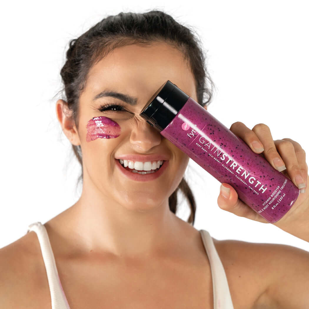 Woman applying Ultra-Nourishing Exfoliating Mask with a happy smile and showing the product bottle.