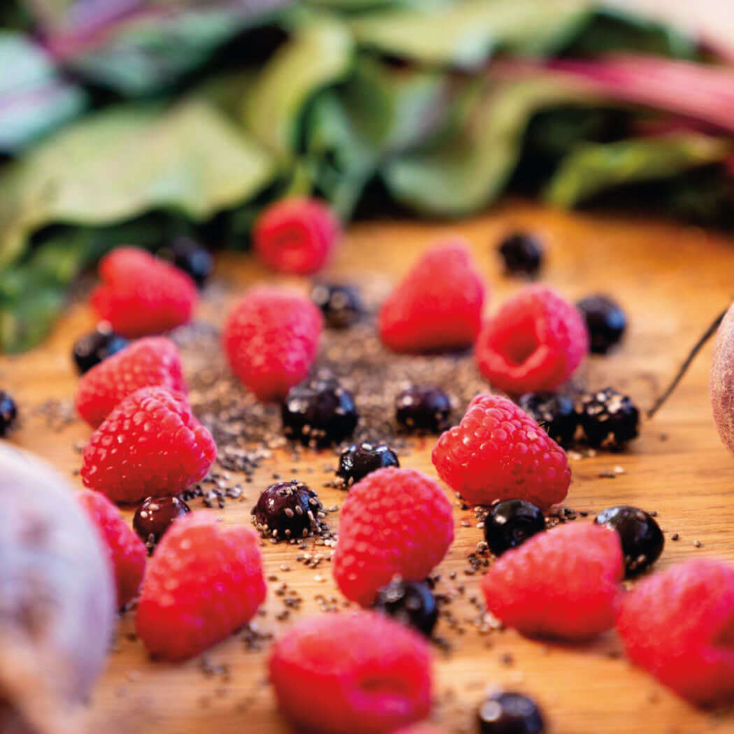 Ultra-Nourishing Exfoliating Mask featuring fresh raspberries and blueberries on a wooden surface surrounded by greens.